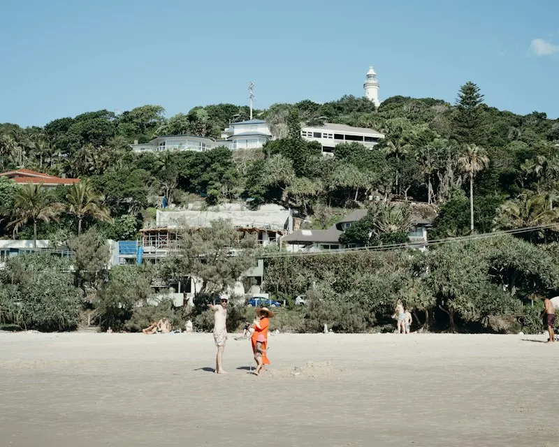 People on the sand at Wategos Beach, with the lighthouse above the trees